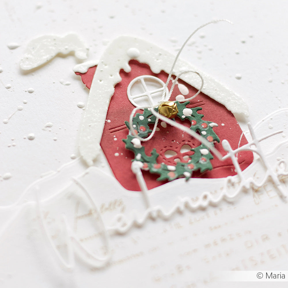 Rotes Papierhaus mit verschneitem Dach, grünem Kranz und goldener Glocke, hergestellt mit Alexandra Renke Motivstanze Lebkuchenhäuschen Dies. Auf weißem Hintergrund. © Maria.