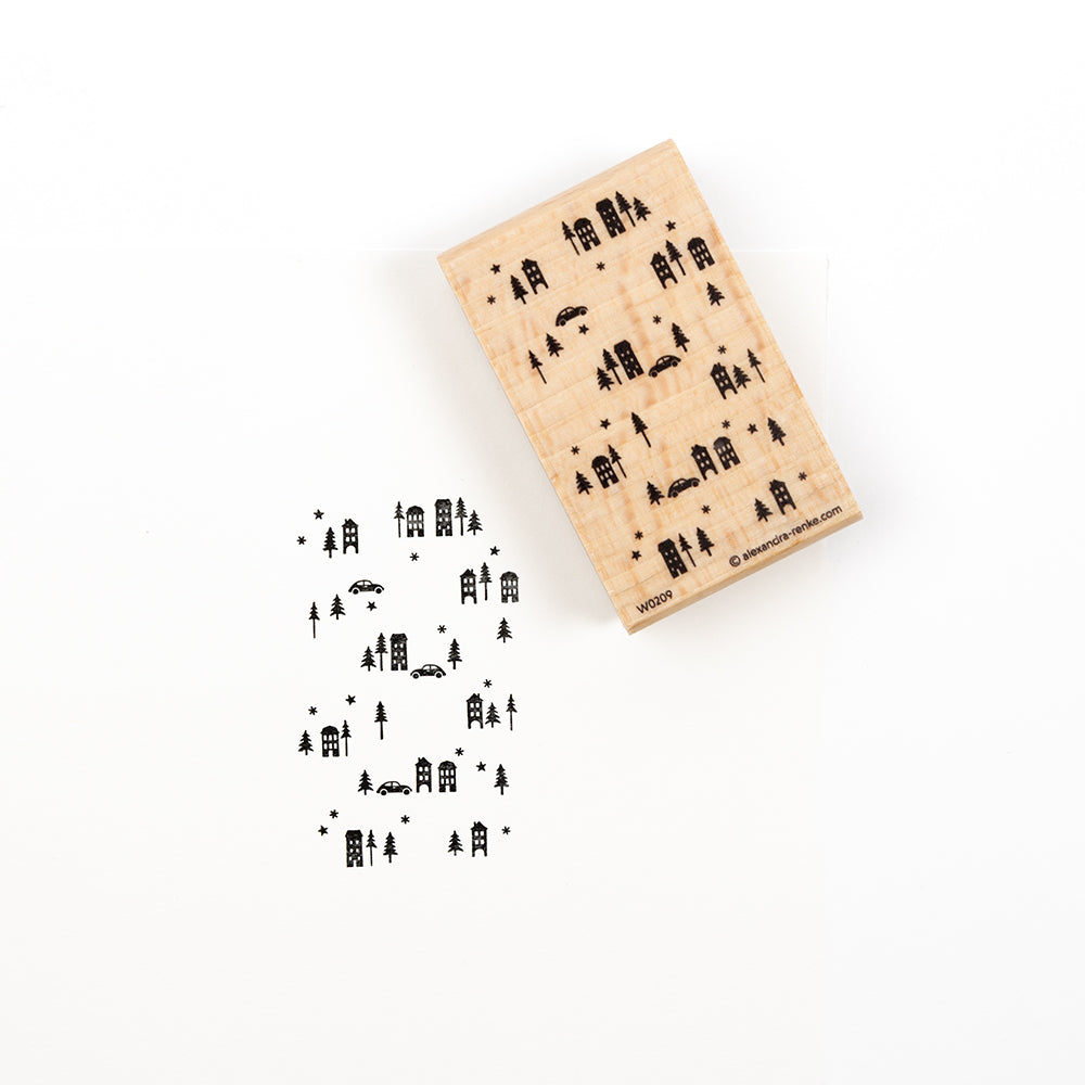 Ein Stempel aus Holz mit einem winterlichen Stadtmotiv im Hintergrund und Baumsilhouetten, unter dem das unten abgebildete Muster eingeprägt ist.