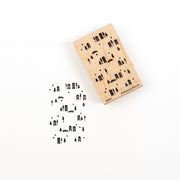 Ein Stempel aus Holz mit einem winterlichen Stadtmotiv im Hintergrund und Baumsilhouetten, unter dem das unten abgebildete Muster eingeprägt ist.