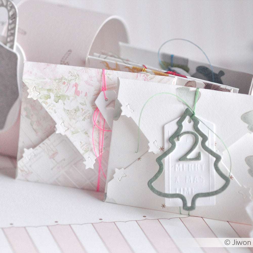 Weißer Umschlag mit Weihnachtsbaumausschnitt aus der Motivstanze Lebkuchen Anhänger Tanne von Alexandra Renke, Sternenkonfetti und pastellfarbener Schnur - ideal zum Basteln mit Ihren Lieblingsdesignpapieren.
