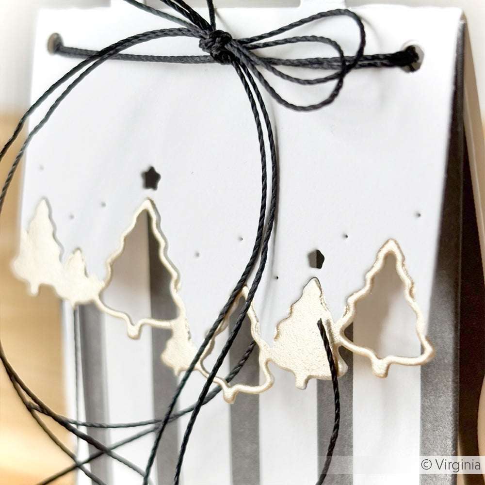 Weiße Geschenktasche mit goldenen Motivstanze-Baumausschnitten von Alexandra Renke, schwarz gestreiftem Designpapier-Hintergrund, Tütengriff Tannenwald und schwarzer Kordelschleife.