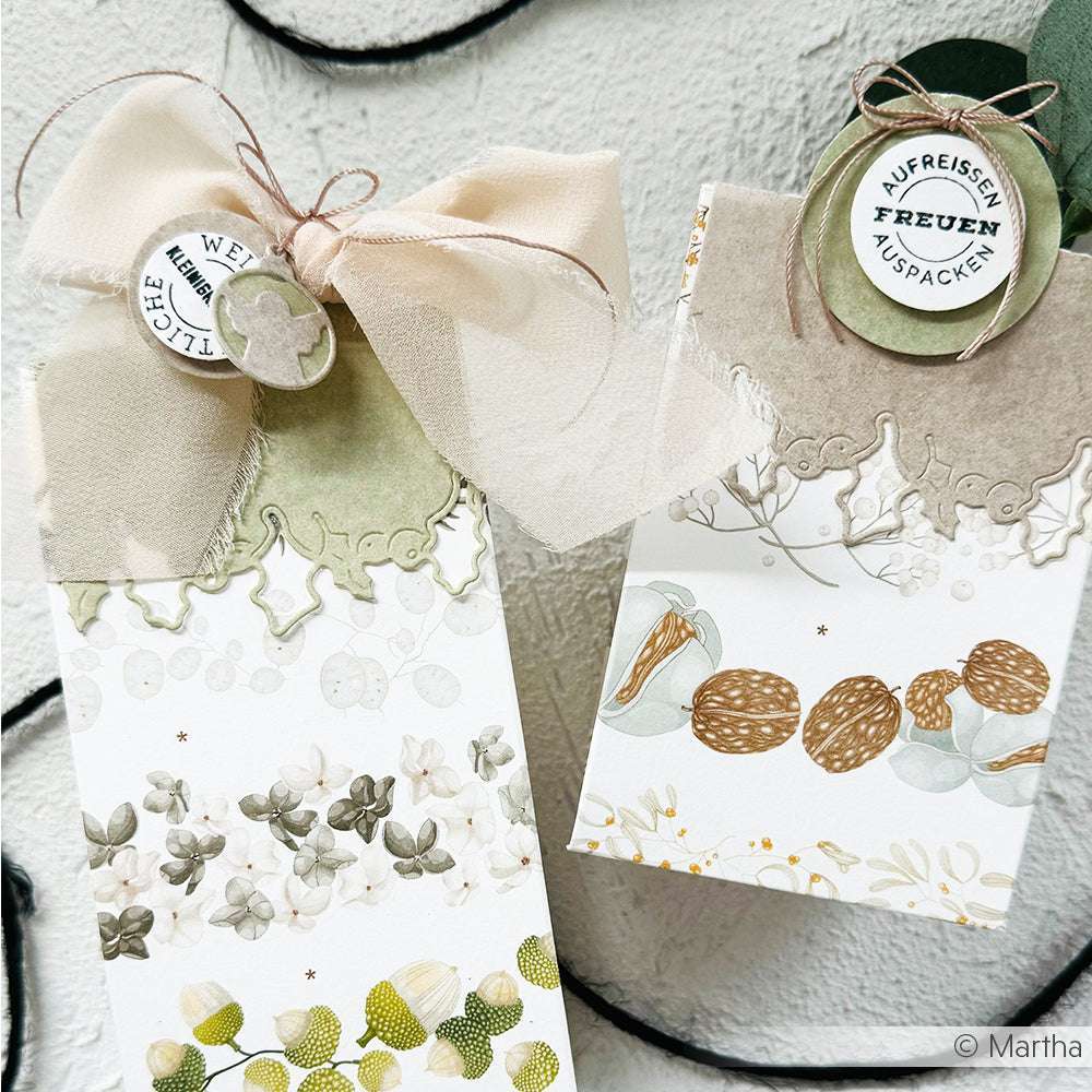 Zwei stilvolle Geschenktüten mit Schleifen, Spitzendetails und floral-nussigem Muster auf hellem Grund, gefertigt aus Alexandra Renke Designpapieren 200g und veredelt mit der Alexandra Renke Motivtanze Tütengriff Ilex.