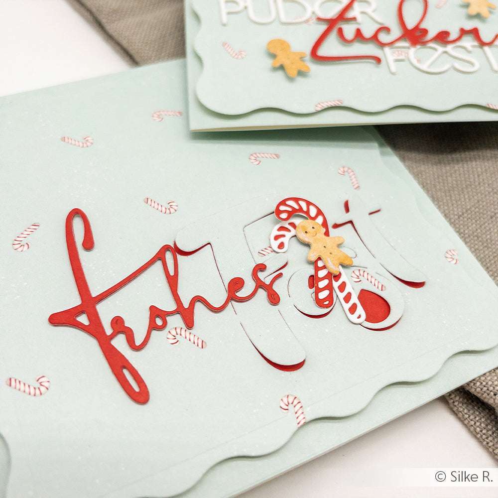 Hellgrüne Weihnachtskarte auf hochwertigen Designpapieren von Alexandra Renke, verziert mit roter Schrift, Zuckerstangen, die mit der Motivstanze Schicht Zuckerstange ausgestanzt wurden, und einer kleinen Lebkuchenfigur.