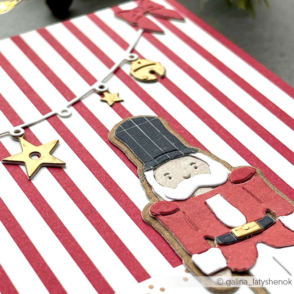 Ein Nussknacker aus Papier und goldene Sterne von Alexandra Renke ruhen auf einem rot-weiß gestreiften Hintergrund, der aus hochwertigem Designpapier gefertigt ist.