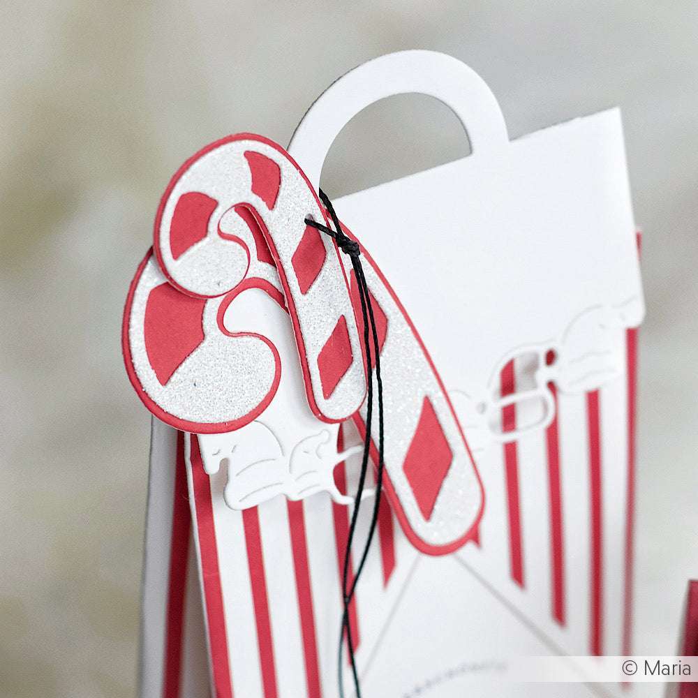 Eine Geschenktüte mit roten und weißen Streifen, verziert mit glitzernden Zuckerstangenanhängern, die mit der Alexandra Renke Motivstanze Schicht Zuckerstangen Duo gefertigt wurden und für einen festlichen Touch sorgen.