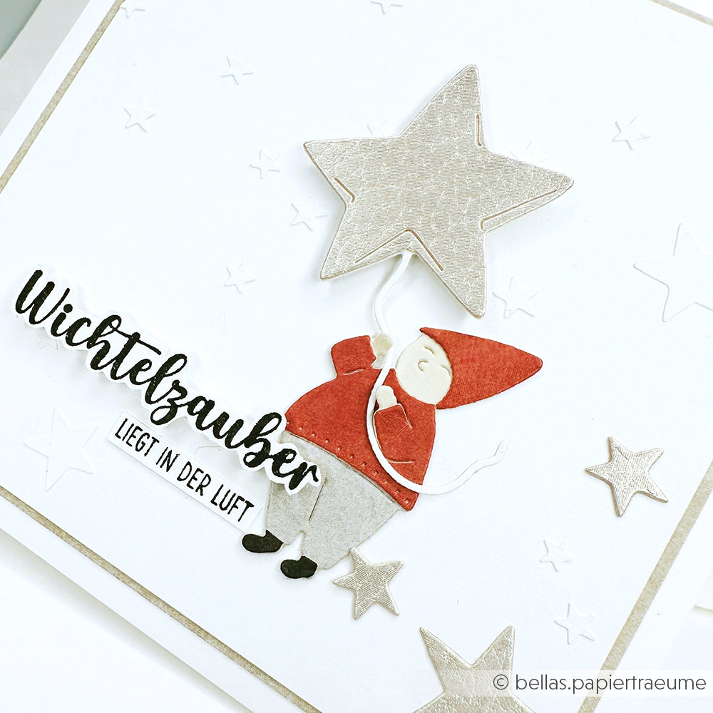 Grußkarte mit einem Wichtel, der einen Sternenballon hält, umgeben von Sternen und deutschem Text. Perfekt für Fans von Alexandra Renke und der Motivstanze Wichtel Sternzauber aus Ihren Lieblingsbastelsammlungen.