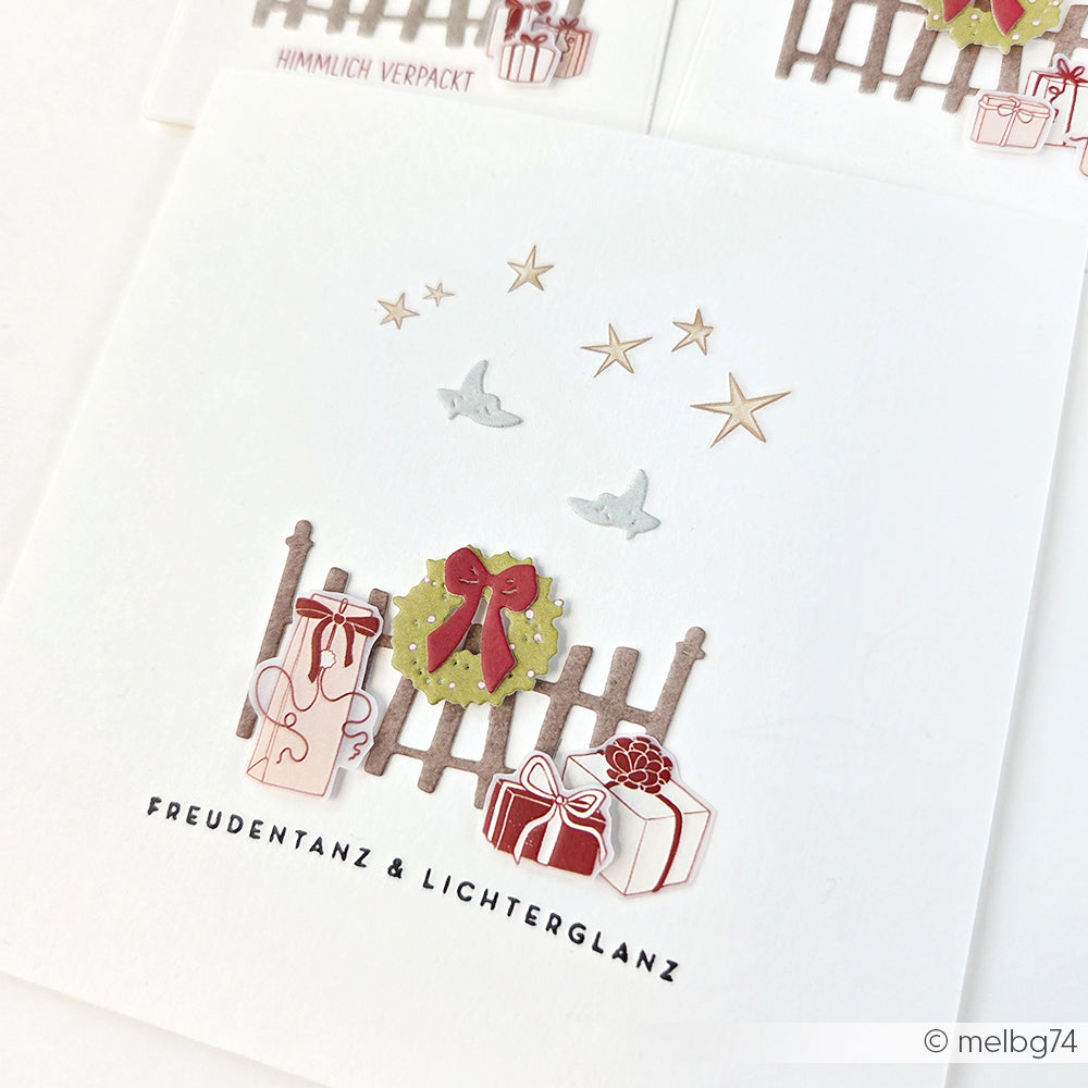 Handgefertigte Weihnachtskarte mit Geschenken, Sternen, Vögeln, einem Holzzaun und einem grünen Kranz, hergestellt mit Alexandra Renke Motivstanze Kleiner Zaun mit Kranz aus 200g Designpapieren - ideal für Stanzen für DieCut Systeme.