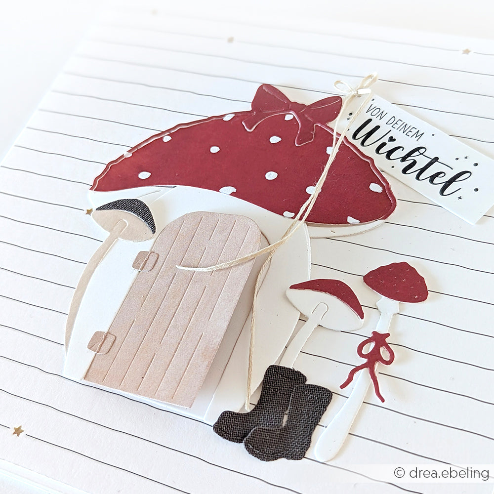 Handgefertigte Karte von Alexandra Renke mit einem rot gefleckten Pilzhaus, kleinen Stiefeln, Pilzen und einem "Von deinem Wichtel"-Tag. Gestaltet mit Designpapieren und der Motivstanze Kleine Tür mit Kranz für charmante Details.