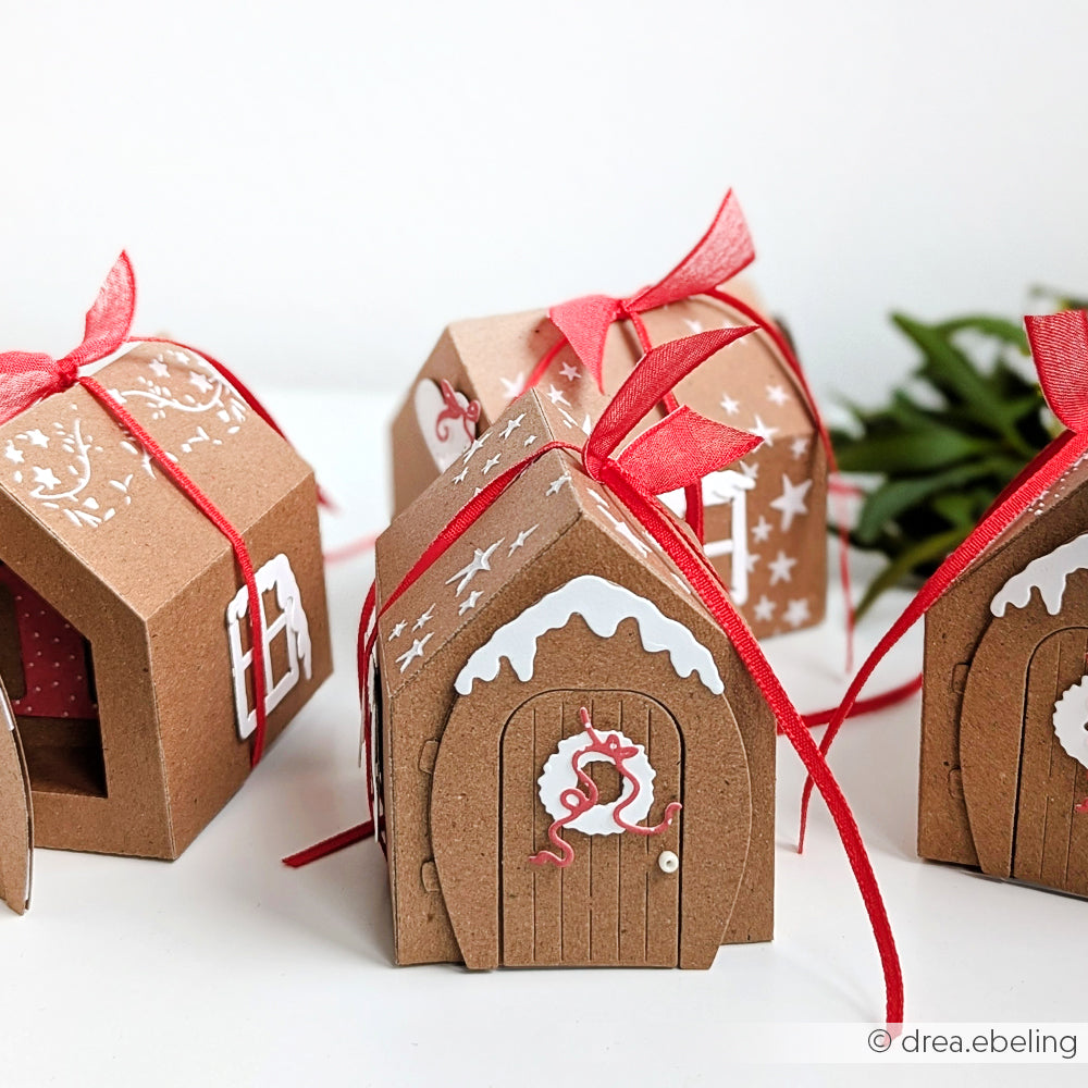 Kleine Lebkuchenhaus-Geschenkboxen aus Pappe von Alexandra Renke mit roten Bändern, weißem Zuckerguss und einer Tür mit Kranz, die mit dem Motivstanze Kleine Tür mit Kranz DieCut System hergestellt wurde - eine bezaubernde festliche Note.