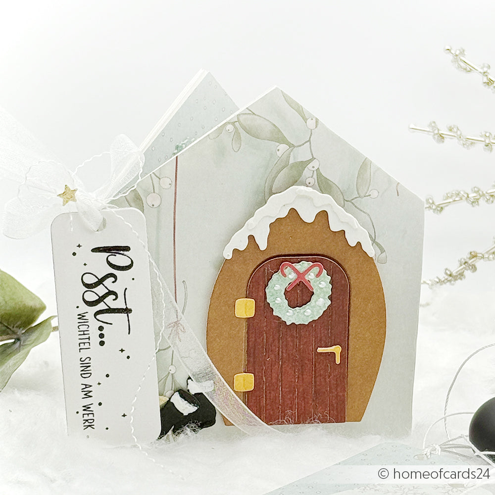 Handgefertigte Weihnachtskarte in Form eines Hauses mit roter Tür, Kranz und verschneitem Dach, hergestellt mit Alexandra Renke Motivstanze Kleine Tür mit Kranz und festlichen Designpapieren, verziert mit einem fröhlichen Anhänger.