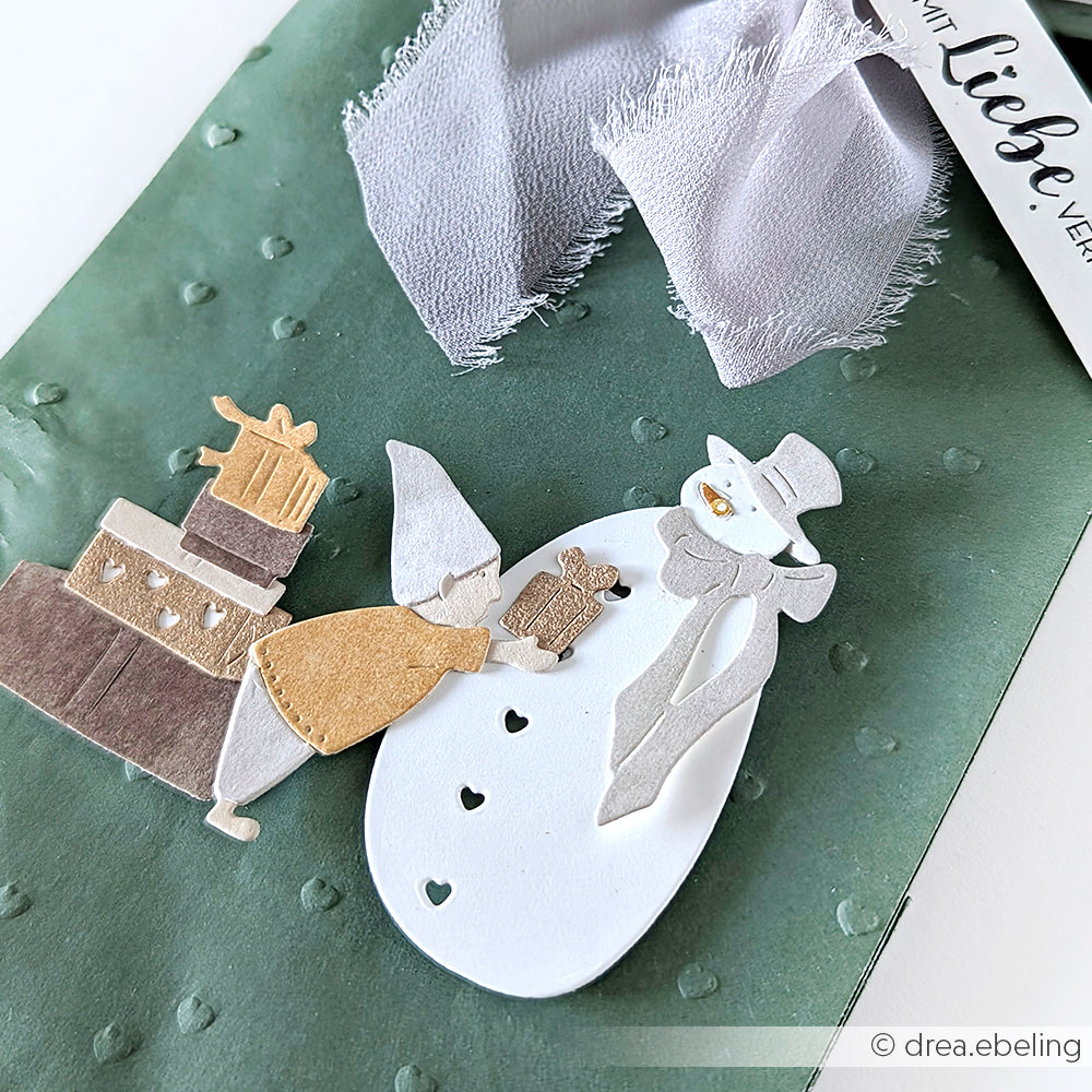 Handgemachte Karte von Alexandra Renke mit einem Mädchen, das einen Schneemann verschenkt, umgeben von Geschenken auf grünem, strukturiertem Hintergrund, hergestellt mit DieCut Systemen und Designpapieren für zusätzlichen Charme.