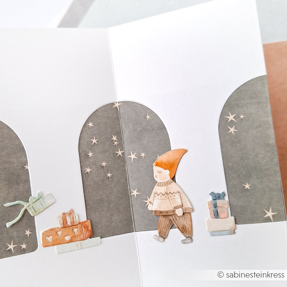 Ein handgezeichneter Elf, gestanzt mit DieCut Systemen und Motivstanze Wichtel am Lagerfeuer von Alexandra Renke, spaziert auf einer leichten Festtagskarte unter Sternenbögen an Geschenken vorbei - ideal für kreative Designpapiere.