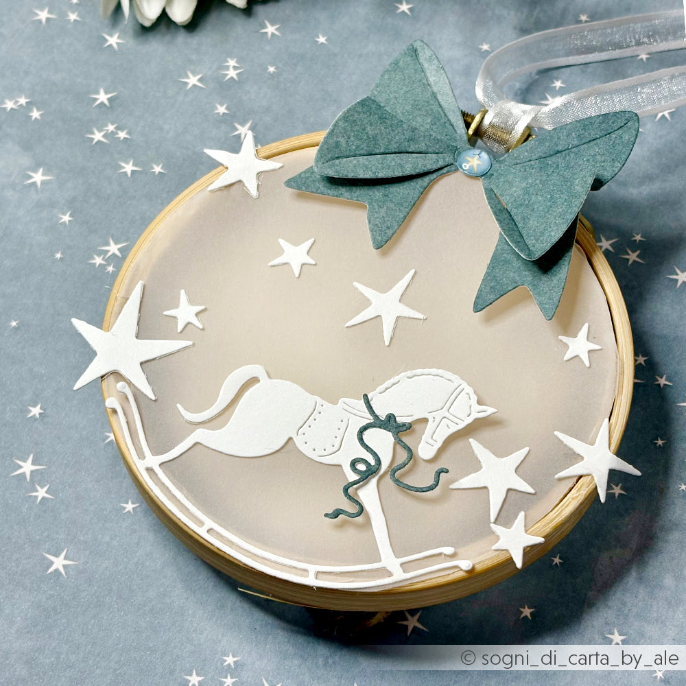 Rundes Ornament mit einem weißen Schaukelpferd, Sternen und einer blauen Papierschleife auf einem sternförmigen Hintergrund, hergestellt mit Alexandra Renke Designpapieren für zusätzlichen Charme.