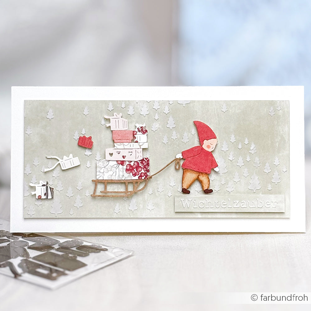 Handgefertigte Karte von Alexandra Renke: Ein Wichtel zieht einen mit Geschenken beladenen Schlitten durch eine verschneite Landschaft mit weißen Bäumen. Perfekt für den Wichtel Geschenke-Lieferdienst - gestaltet mit filigraner Motivstanze und passenden Stanzsystemen.