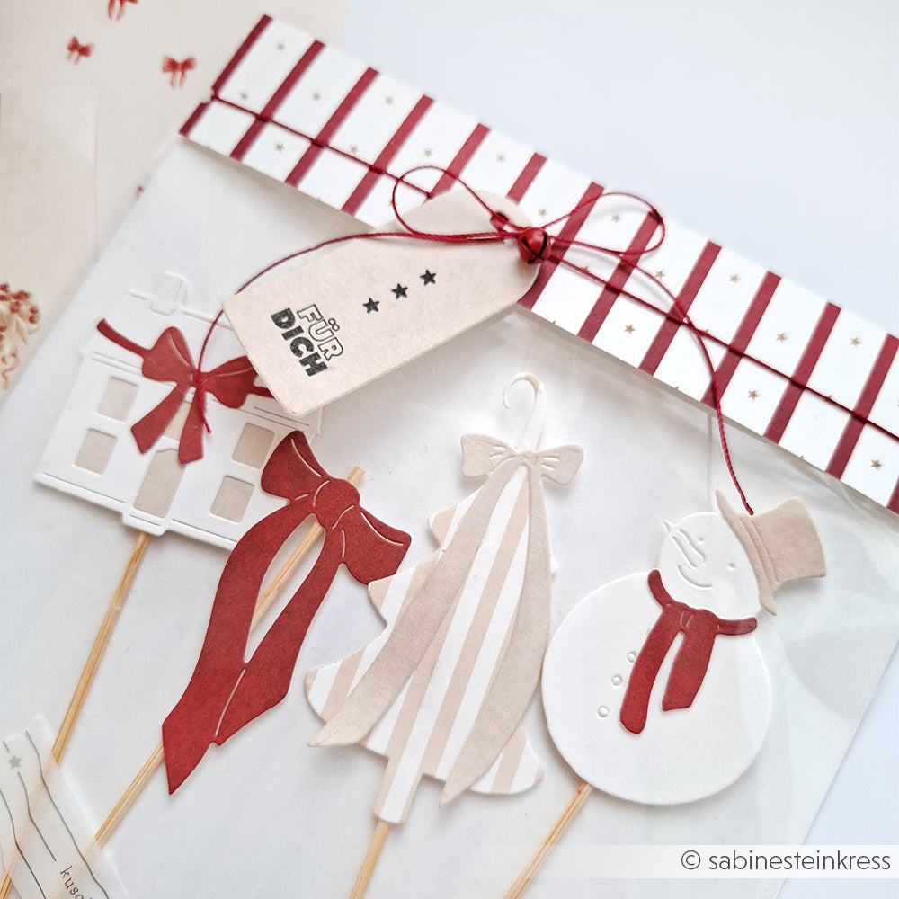 Weihnachtsschmuck aus Papier - ein Haus, zwei Bäume und ein Schneemann - hergestellt mit Alexandra Renke Dies und Motivstanze Schneemann, verziert mit rotem Band und Geschenkanhänger.
