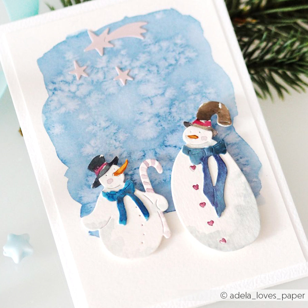 Zwei aquarellierte Schneemänner mit Schals und Mützen, die mit den Alexandra Renke Fröhlicher Schneemann Stanzformen hergestellt wurden, stehen unter Sternschnuppen auf einer festlichen Winterkarte.