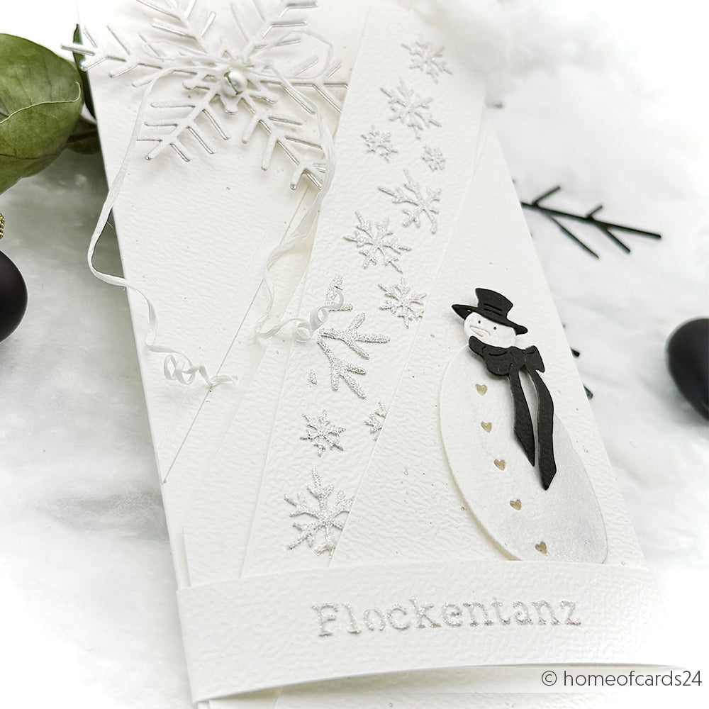 Weiße, handgefertigte Karte von Alexandra Renke Designpapiere mit Schneeflockenmotiven, einem gestanzten Schneemann und dem in Silber geprägten "Flockentanz".