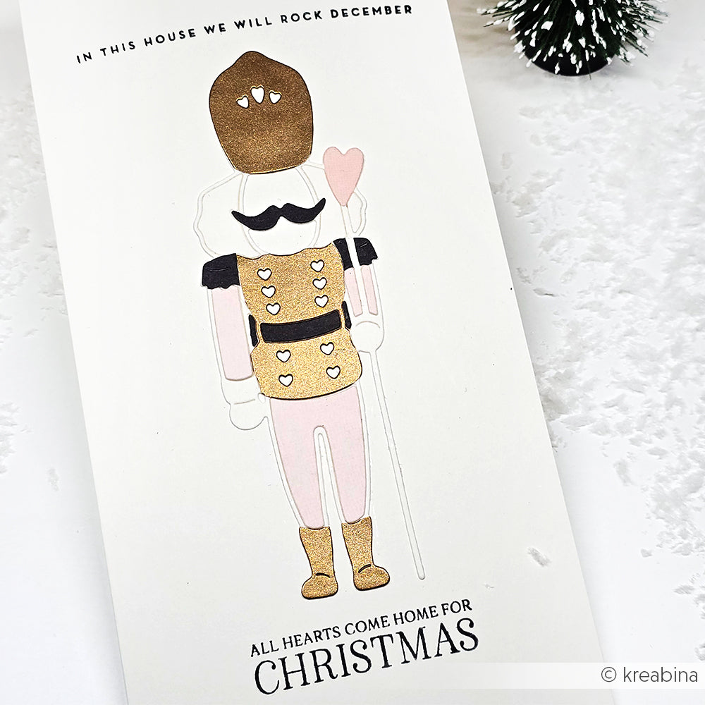 Eine festliche Karte von Alexandra Renke mit einem Nussknacker, goldenen und rosafarbenen Akzenten, hergestellt mit Motivstanze Lieblings-Nussknacker und hochwertigem Designpapier. Mit der Botschaft "Alle Herzen kommen zu Weihnachten nach Hause".