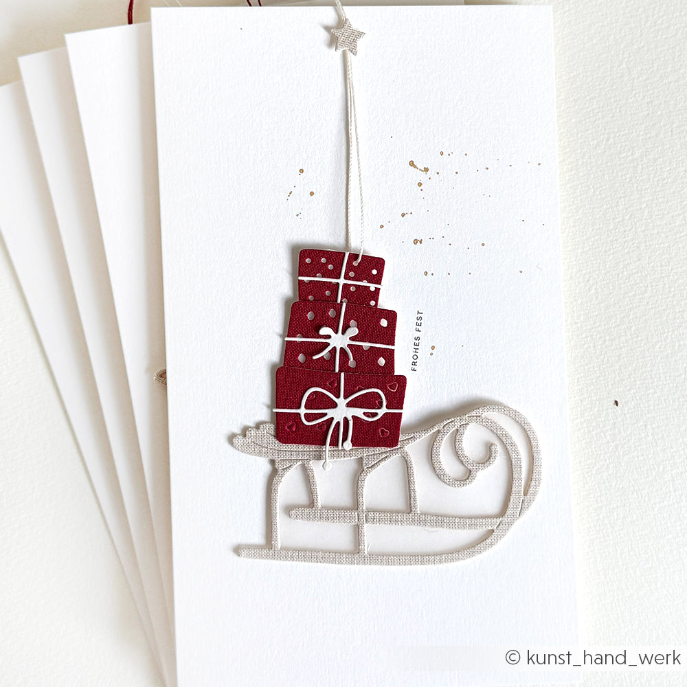 Grußkarte von Alexandra Renke mit einem großen Schlitten als DieCut-Motiv, der rote Geschenkschachteln mit weißen Schleifen auf einem strahlend weißen Hintergrund trägt - ein bezauberndes Design, das mit DieCut Systeme Stanzen hergestellt wurde.
