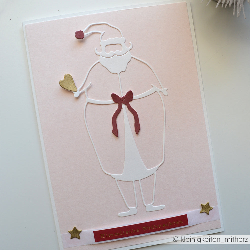 Minimalistischer weißer Weihnachtsmannausschnitt mit der Motivstanze Weihnachtsmann von Alexandra Renke, die eine rote Schleife, ein goldenes Herz und zwei goldene Sterne auf hellem Hintergrund zeigt.