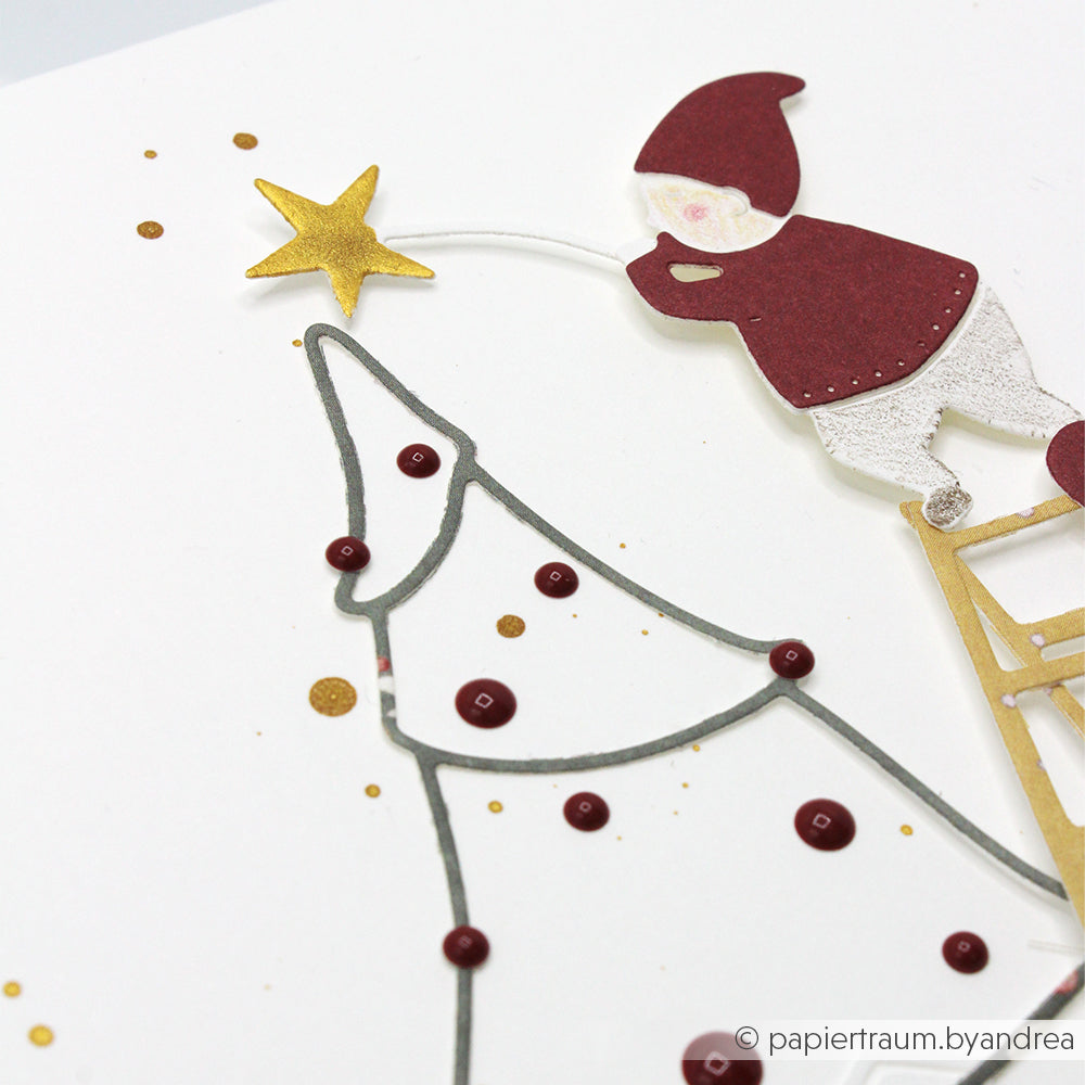 Eine handgefertigte Karte von Alexandra Renke zeigt eine Elfe, die einen goldenen Stern auf einen minimalistischen Tannenbaum aus Motivstanze setzt - perfekt, um Weihnachtsstimmung zu verbreiten.