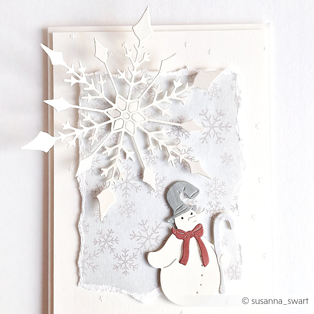Handgemachte Karte von Alexandra Renke mit einer Papierschneeflocke aus der Motivstanze Große Schneeflocke und einem Schneemann mit rotem Schal auf einem frostigen silbernen Hintergrund.