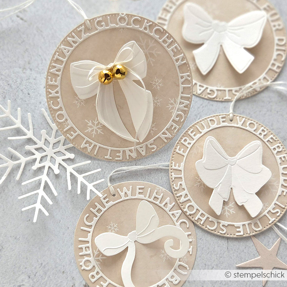 Alexandra Renke runde beigefarbene Ornamente mit weißen Schleifen, deutschem Text, goldenen Glocken und Schneeflocken, gestanzt mit der Motivstanze Große Schneeflocke auf grau, hergestellt aus 200g Designpapieren mit Stanzen aus Stahl.