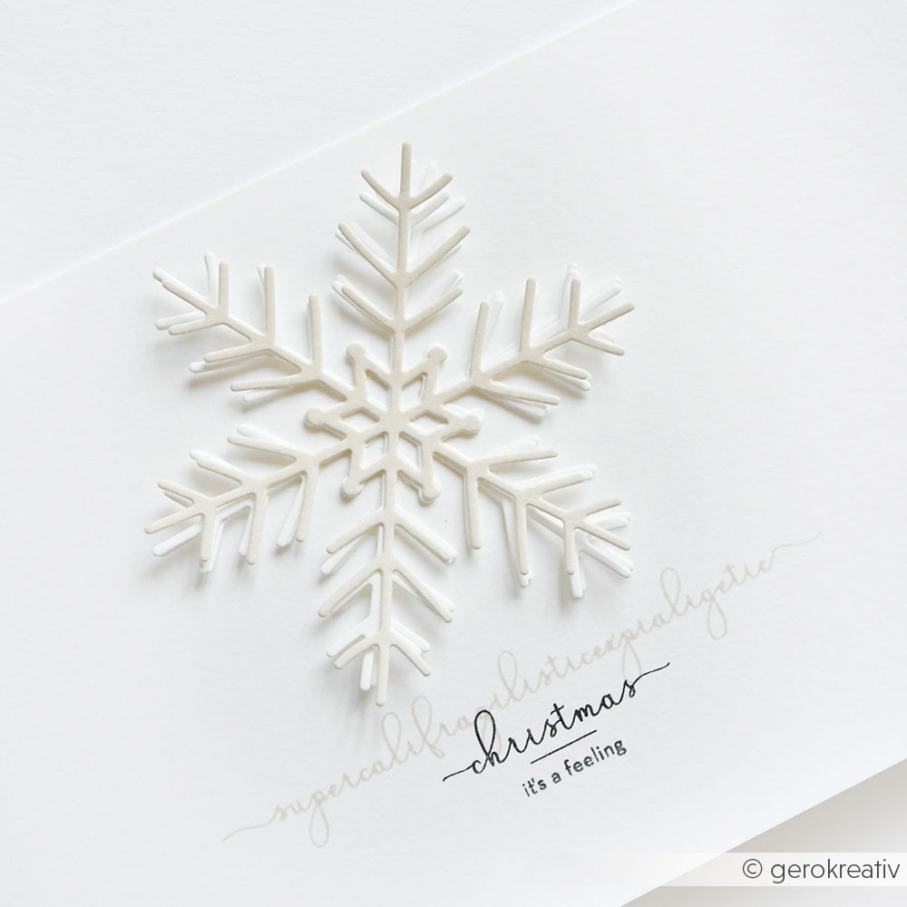 Eine weiße Schneeflocke, gestaltet mit Alexandra Renke's Große Schneeflocke Stanzsysteme, ziert eine weiße Karte. Darunter steht "Weihnachten, das ist ein Gefühl" auf hochwertigen Alexandra Renke Designpapieren.