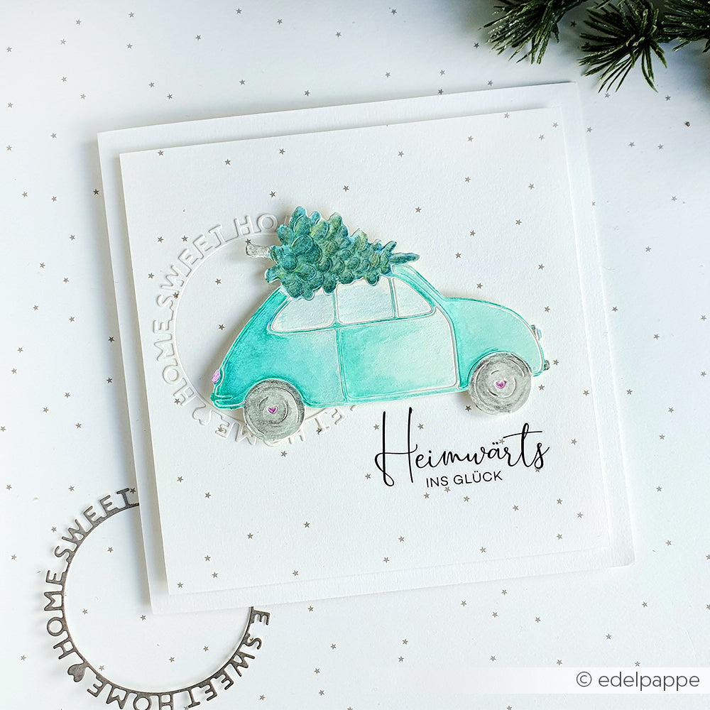 Eine Karte mit einem tealfarbenen Auto, das einen Weihnachtsbaum trägt, hergestellt mit der Alexandra Renke Motivstanze Auto mit Tanne und dem deutschen Text "Heimwärts ins Glück". Ideal für kreative Projekte mit Alexandra Renke Designpapieren und Stanzsystemen.