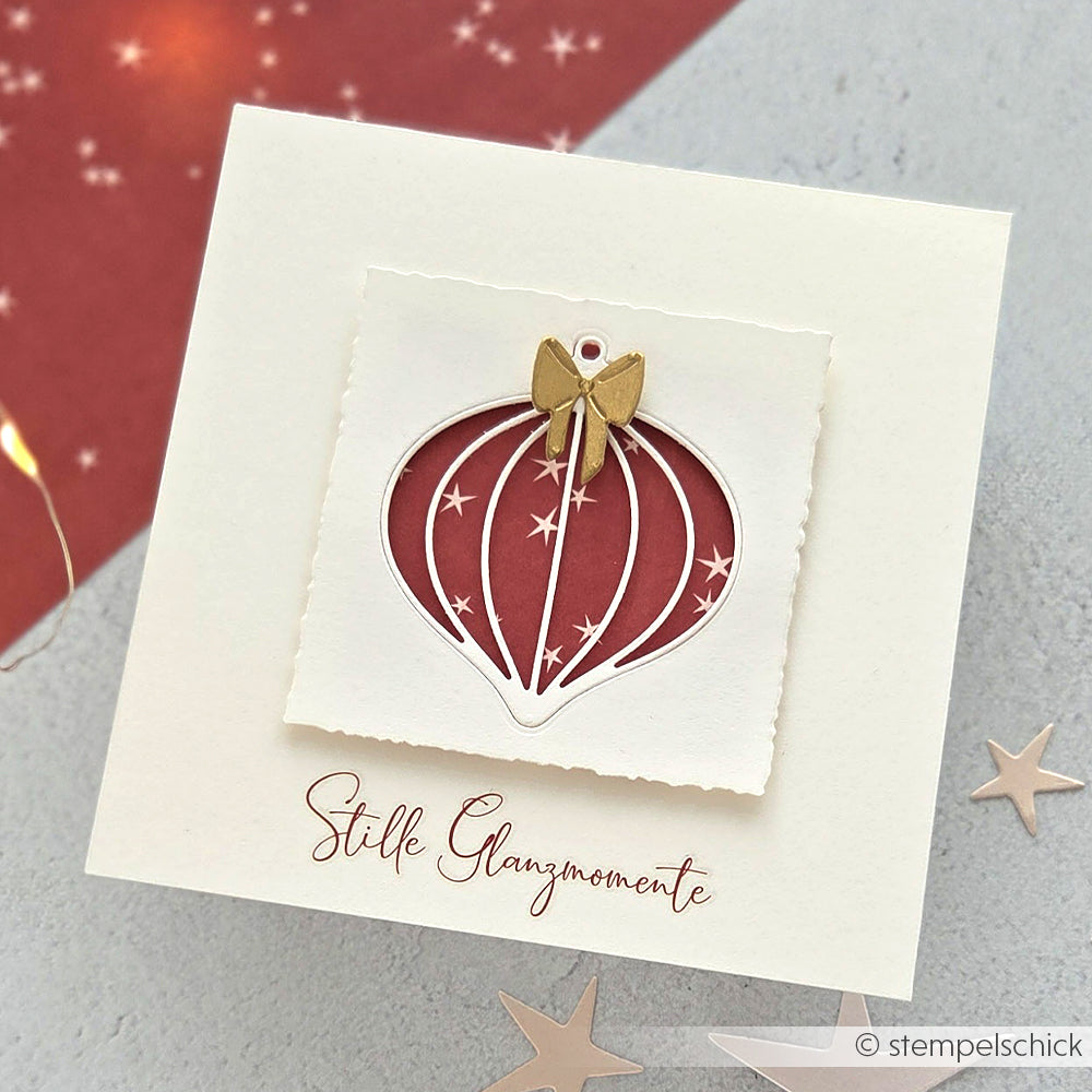 Quadratische Weihnachtskarte von Alexandra Renke mit goldener Schleife, Ornamentausschnitt aus der Motivstanze Feine Weihnachtskugel, rotem Hintergrund und deutschem Text darunter.