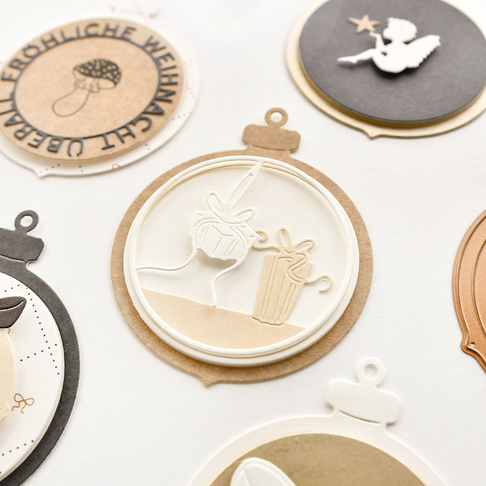 Neutraler und weißer Lagenpapierschmuck von Alexandra Renke aus hochwertigen Designpapieren mit weihnachtlichen Motiven - Geschenke, ein Pilz und ein Engel - erstellt mit Stanzsystemen und Motivstanze Klappbare Christbaumkugel für festliche Dekoration.