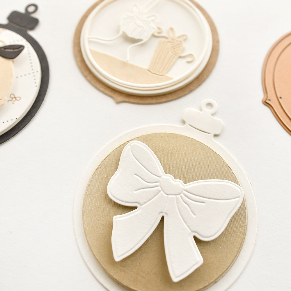 Kreisförmige Papierornamente mit geschichteten Cut-Out-Motiven von Alexandra Renke, gefertigt aus hochwertigen Designpapieren und Stanzsystemen, mit einer auffälligen weißen Schleife im Vordergrund.