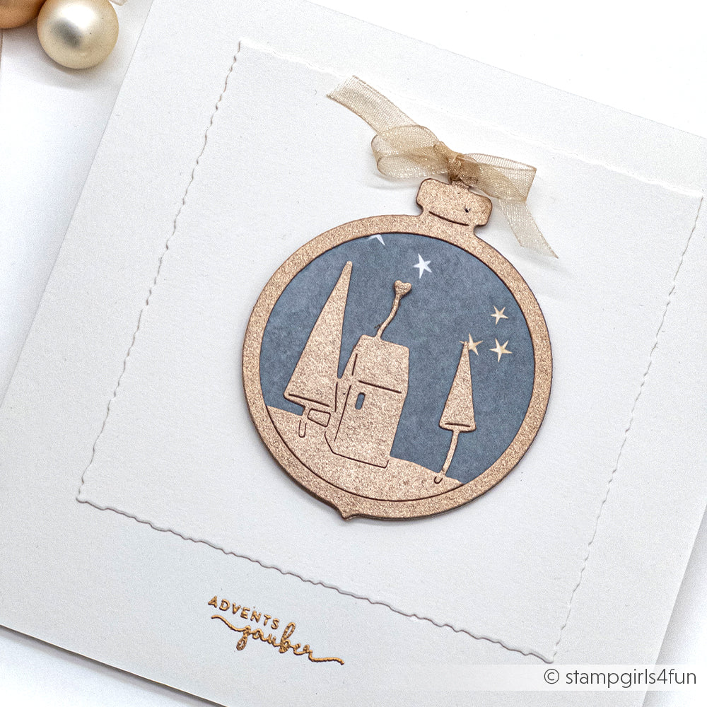 Handgefertigte Weihnachtskarte von Alexandra Renke mit einem goldenen Ornament aus der Motivstanze Klappbare Christbaumkugel, mit Bäumen, einem Haus und Sternen auf blauem Designpapier.