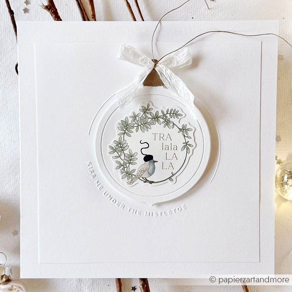 Quadratische weiße Weihnachtskarte von Alexandra Renke mit einer Kugel, einem Blumenmuster und "TRALALALALA", hergestellt mit der Motivstanze Klappbare Christbaumkugel. Auf der Karte steht: "KÜSS MICH UNTER DEM MISTELZWEIG.