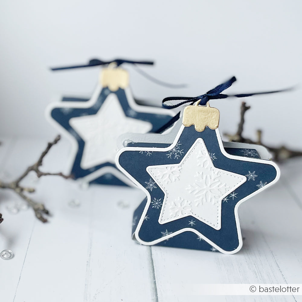 Zwei sternförmige Geschenkboxen mit marineblauen und weißen Schneeflocken-Sternmustern.
