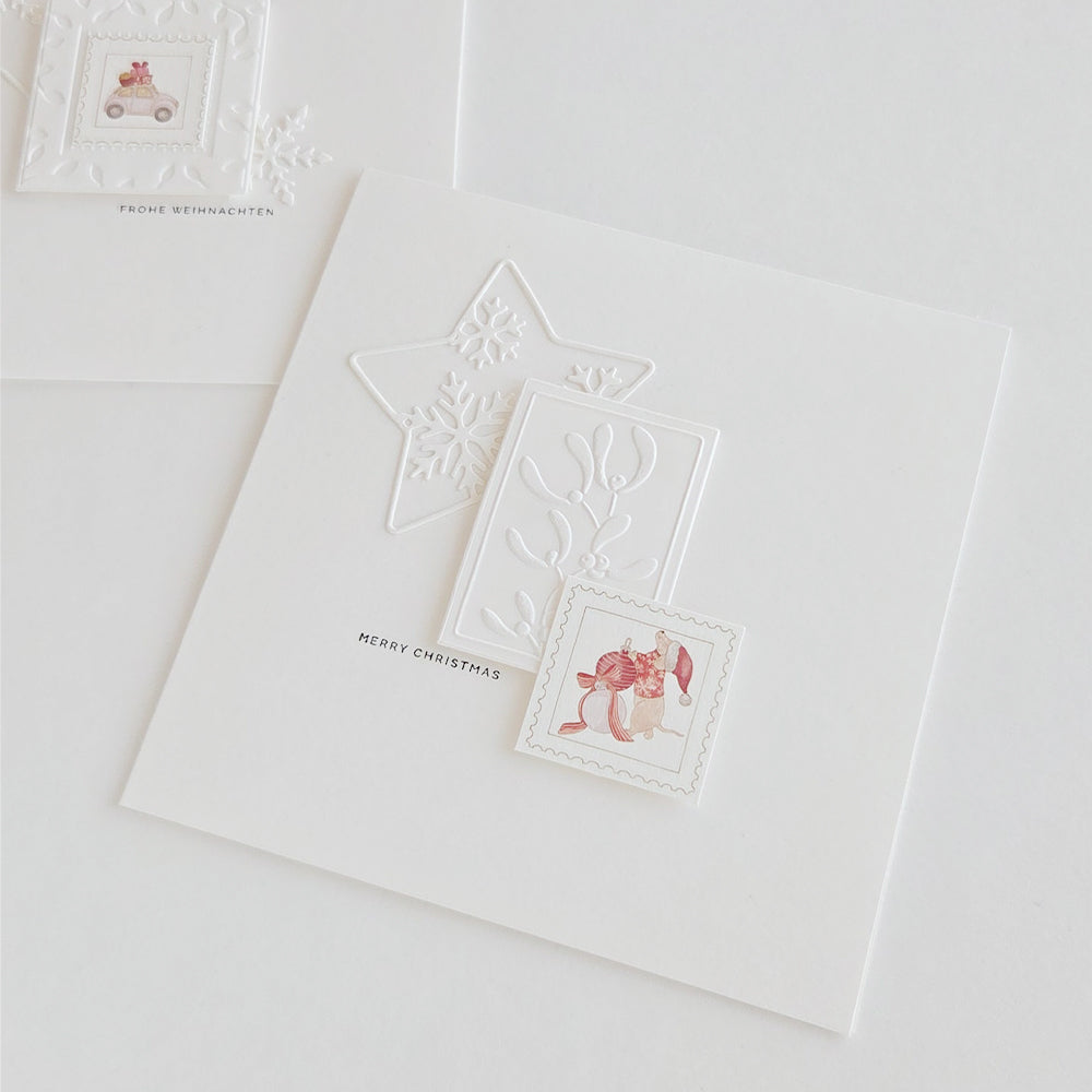 Weiße Weihnachtskarten mit geprägten Stern- und Schneeflocken-Motiven im Stanzstil und einer kleinen illustrierten Maus, die einen Christbaumschmuck in der Hand hält.