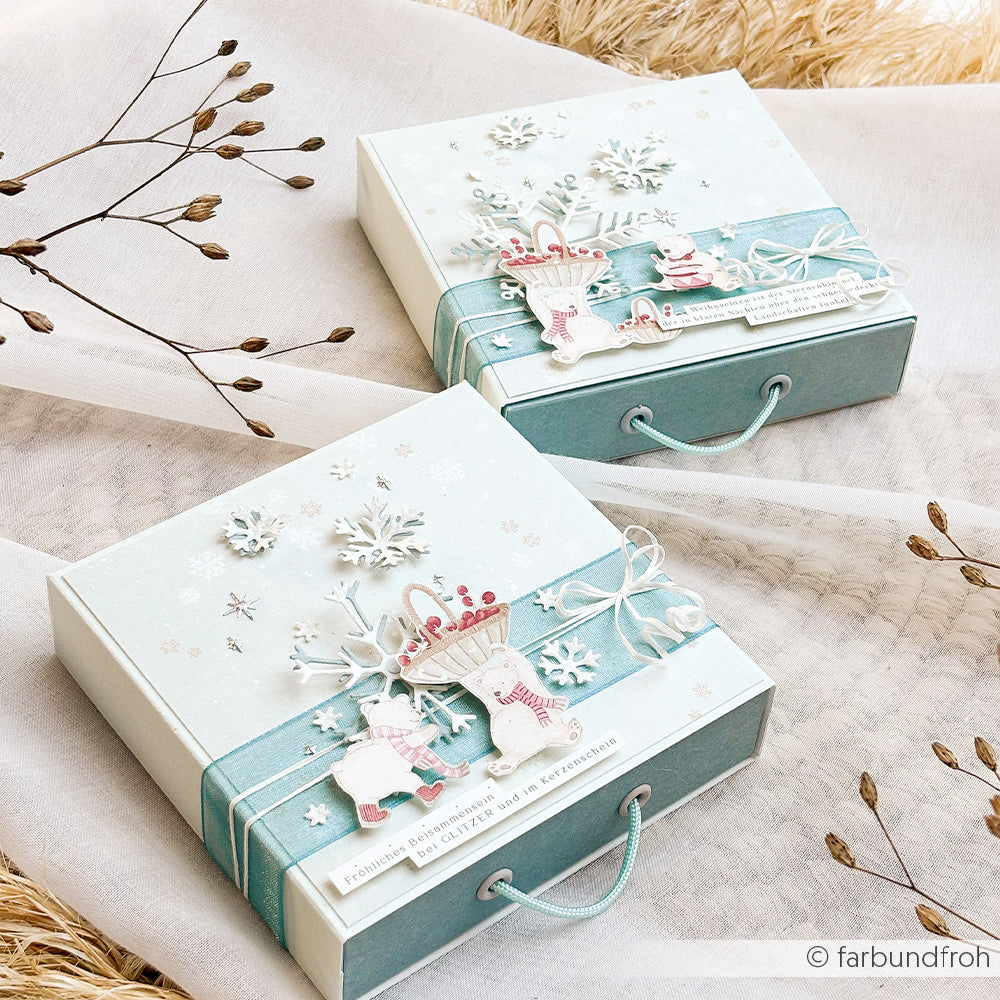Zwei hellblaue Geschenkboxen, verziert mit ausgestanzten Schneeflockenmotiven und Bändern.