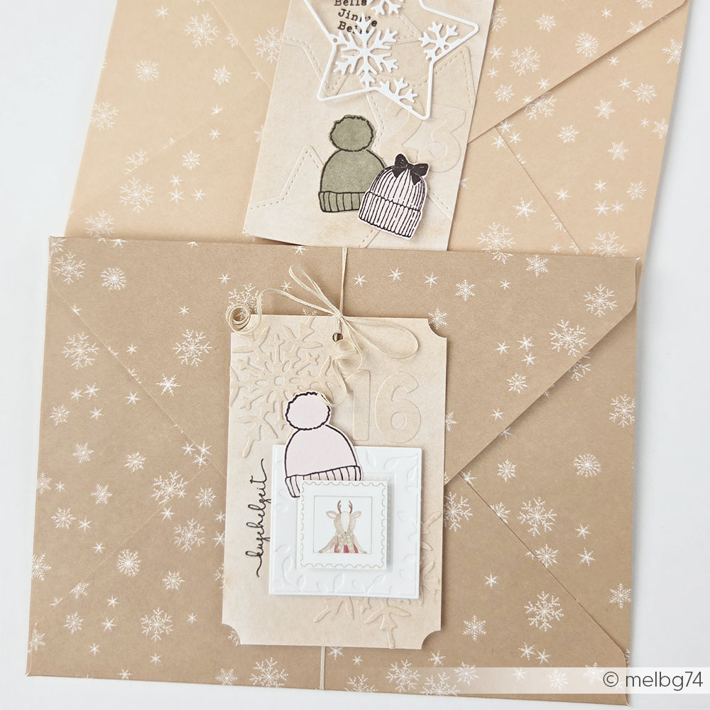 Zwei hellbraune Umschläge mit Schneeflocken-Motiv, verziert mit Papieranhängern und Wintermützen.