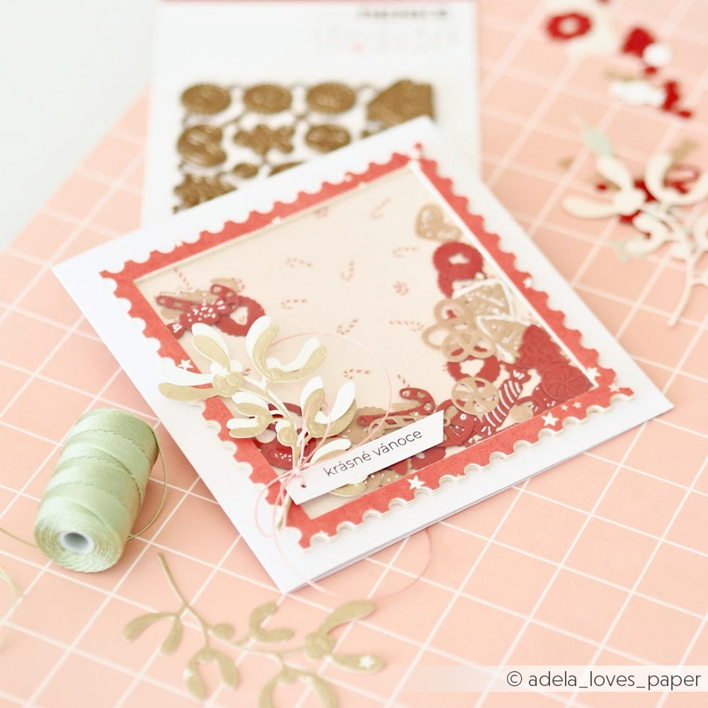 Eine handgefertigte Weihnachtskarte mit einem gewellten roten Rahmen, Mistelzweigen und dekorativen Designpapieren.