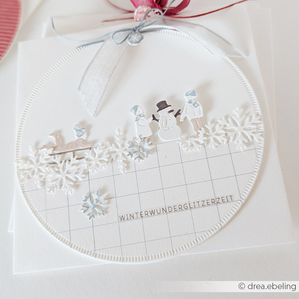 Handgefertigte Karte mit einer Winter-Spa-Szene, verziert mit Papierausschnitten eines Schneemanns, zweier Personen und Schneeflocken.