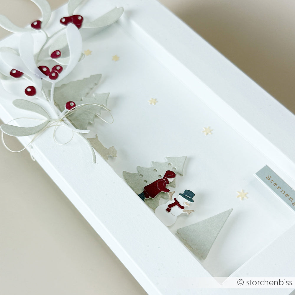 Shadow-Box-Kunst mit einer Winterspaß-Szene, in der ein Kind einen Schneemann baut, mit Mistelzweig und immergrünen Pflanzen.