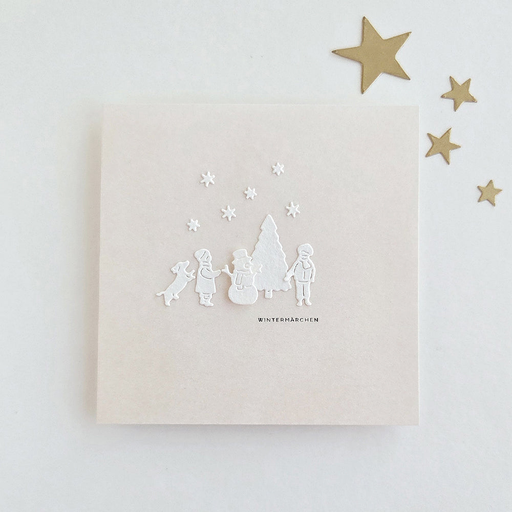Eine Karte mit einer weißen, geprägten „Winterspaß“-Szene, auf der Kinder, ein Hund, ein Schneemann und ein Baum zu sehen sind, sowie dem Schriftzug „WINTERMÄRCHEN“.