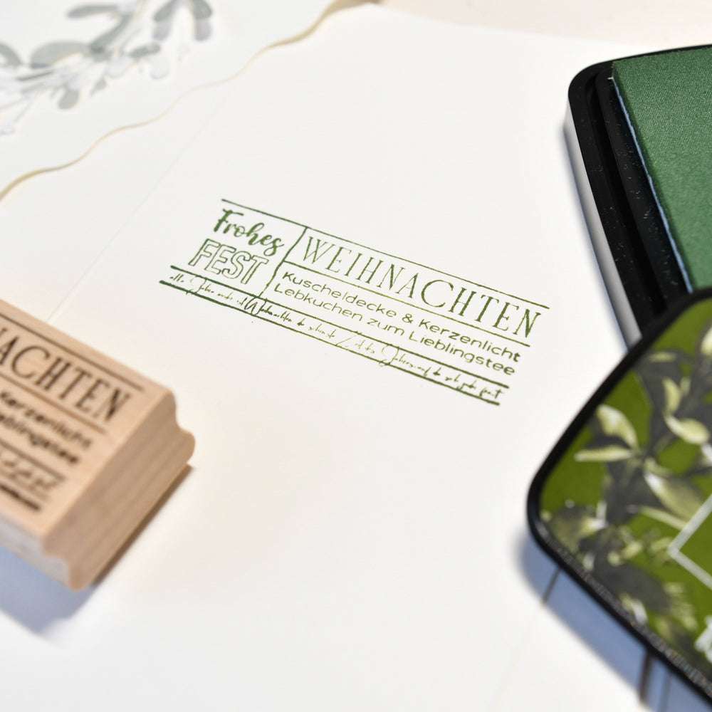 Rubber Holzstempel von Alexandra Renke mit "Frohes Fest Weihnachten" auf weißem Papier gestempelt, Stempelkissen in der Nähe - ideal für festliche Karten bei Kerzenschein unter einer kuscheligen Decke.