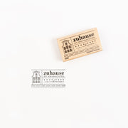 Ein Holzstempel und sein Abdruck mit einem Haussymbol und einem deutschen Text.