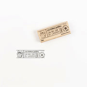 Ein Holzstempel, der eine Geschenkbox und einen deutschen Text neben dem Stempelabdruck zeigt.