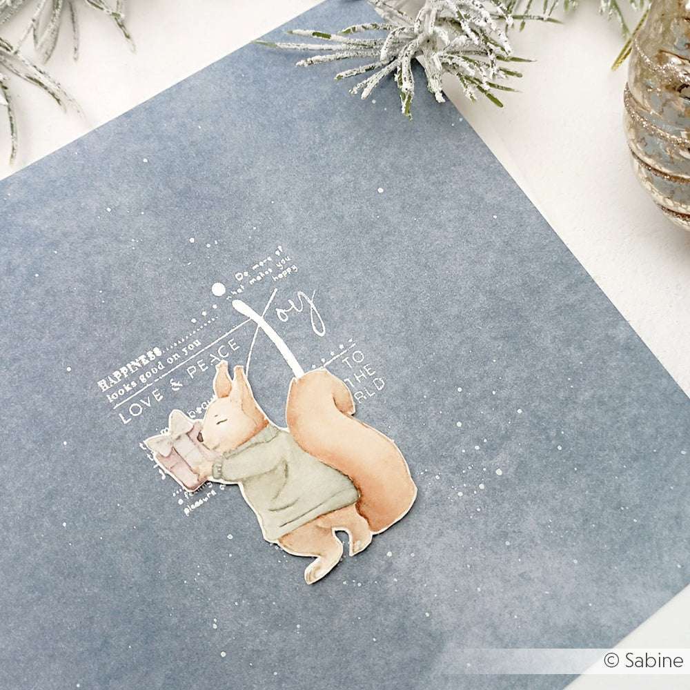 Aquarellierte Eichhörnchen in kuscheliger Kleidung tauschen ein Geschenk auf einer blauen Karte mit Winterdekoration aus - eine perfekte Inspiration für Alexandra Renke Papierprojekte oder für Ihre Lieblingsdesigns mit Holzstempeln und Stempelgummi.