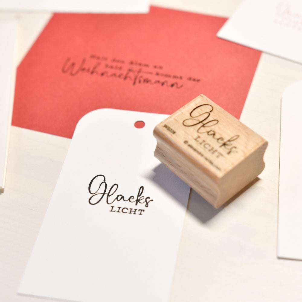 Ein Alexandra Renke Holzstempel und gestempelte Geschenkanhänger liegen auf einem Tisch mit rot-weißen Karten - ideal für kreative Papierprojekte.