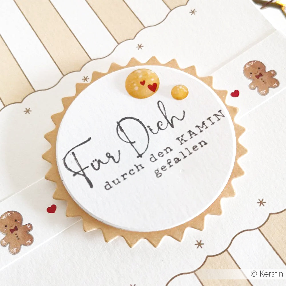 Ein Holzstempel mit der Aufschrift Für Dich durch den Kamin gefallen, umgeben von Lebkuchenmännchen.