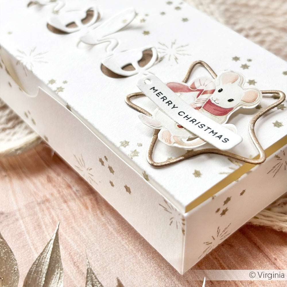 Weiße Geschenkschachtel mit goldenen Sternen, verziert mit einer Maus und einem "Frohe Weihnachten"-Anhänger, verziert mit einem Alexandra Renke Mini Leuchtstrahlen Akzent-Stempel auf einer Holzoberfläche.