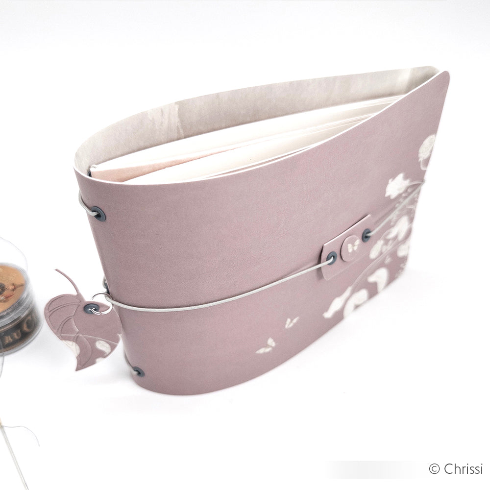 Ein lilafarbenes, floral gemustertes Plaid Enterprises Journal mit gewölbtem Einband und silbernem Verschluss, beschichtet mit Hard Coat für zusätzliche Haltbarkeit, von oben gezeigt.